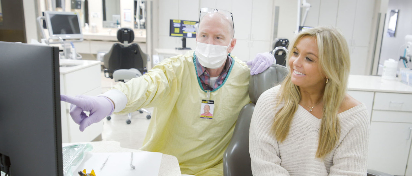 A patient listens while her dentist explains something while pointing to a screen.